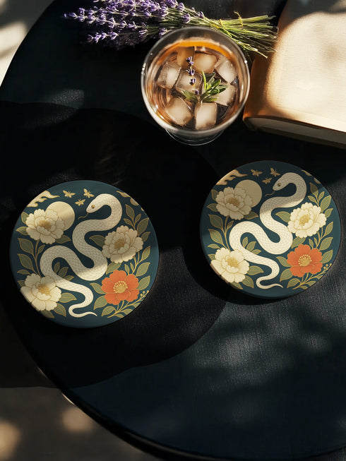 Round ceramic coaster with a chinoiserie-inspired design featuring a white snake among golden peonies, butterflies, and a glowing moon on a dark green background. Surrounded by floral and botanical accents with a soft vintage aesthetic. The coaster has a cork back and measures about 4 inches in diameter. Ideal for mugs, teacups, or wine glasses, this decorative piece suits witchy, victorian, and chinoiserie-inspired decor.